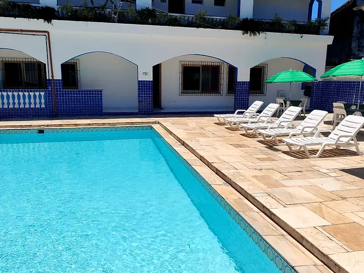 Piscina adulto com espreguiçadeiras brancas e guarda-sóis verdes