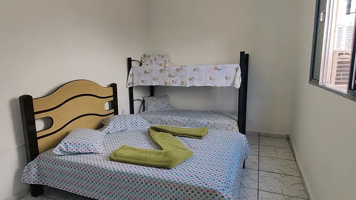 Quarto com cama de casal, beliche e toalhas dobradas sobre a cama