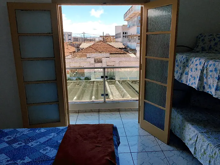 Quarto com beliche e cama, com a porta aberta para a sacada