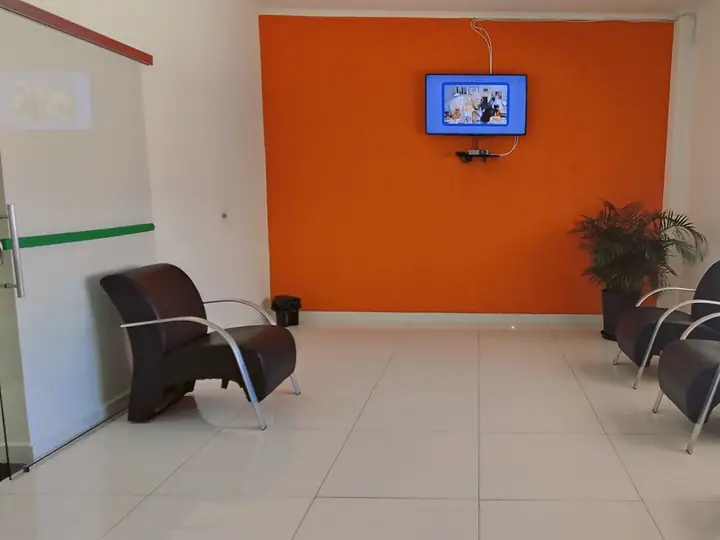 Sala de estar com poltronas, parede laranja e televisão