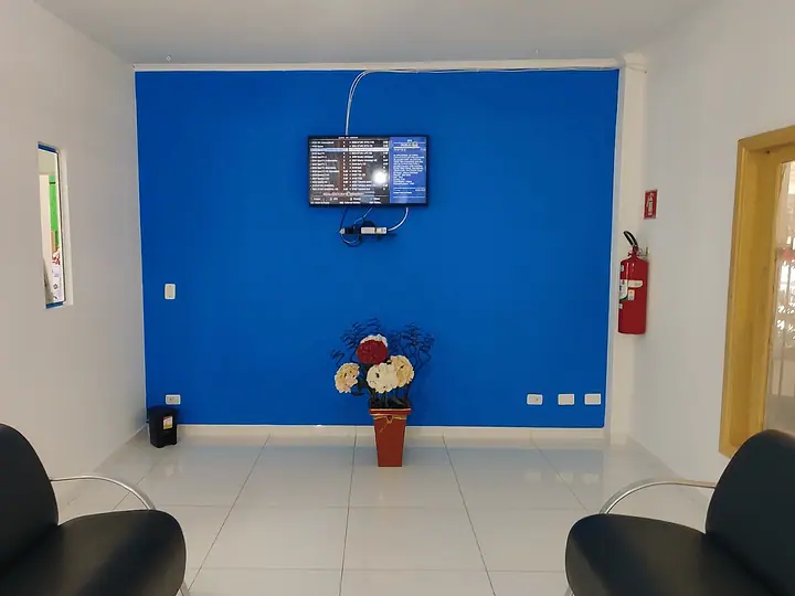 Sala de estar com sofás pretos, parede azul e televisão