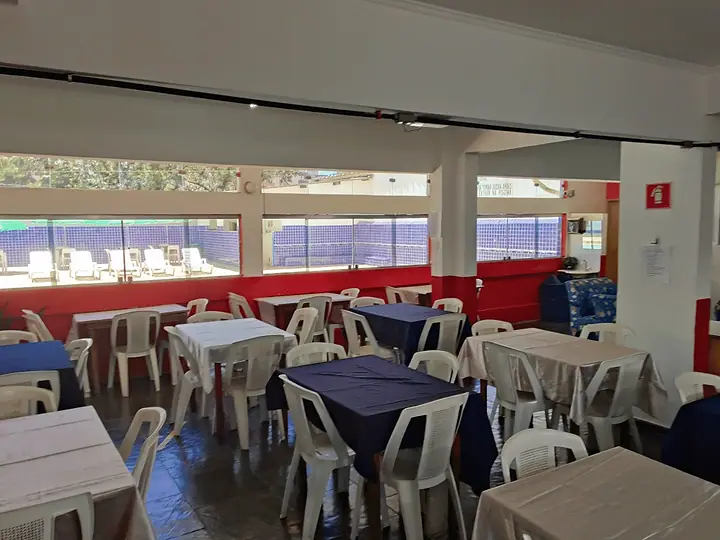 Salão do restaurante com mesas e cadeiras e janelas para a área da piscina